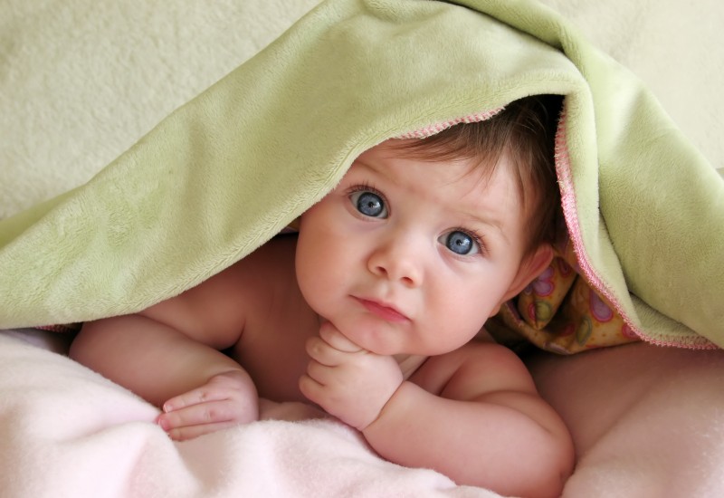 young baby with blue eyes under a green blanket on a pink duvet