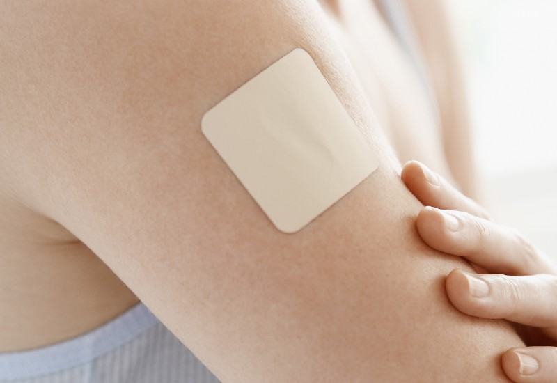 white female holding left arm with right hand. The left arm as a nicotine patch stuck to its bicep.