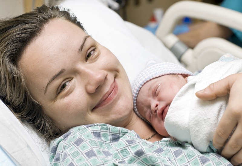 Smiling white mother lying in a hospital bed and anew born baby in on her chest.