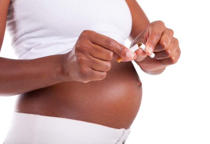 Pregnant black female, with exposed stomach, breaking a cigarette in half.